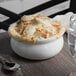 A white Tuxton onion soup bowl filled with food on a table.