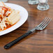 A WNA Comet Reflections Duet stainless steel look plastic fork in black on a plate of pasta.