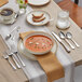 A table set with a bowl of soup, a butter spreader, and silverware.