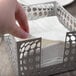 A hand picking up a napkin from a Clipper Mill gray powder coated iron napkin holder.
