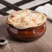 A close up of a Tuxton caramel onion soup crock filled with food with a spoon on the table.