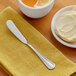 An Acopa stainless steel butter spreader on a plate with a bagel and butter.