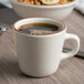 A Tuxton brown speckle tall china cup filled with coffee on a table with a bowl of cereal.
