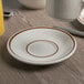 A Tuxton Bahamas brown speckle saucer with a brown rim on a wooden table.