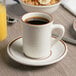 A cup of coffee on a Tuxton Bahamas brown speckle saucer on a table with a bowl of fruit.