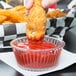 a person holding a chicken nugget over a bowl of ketchup