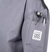 A close-up of a Chef Revival unisex gray long sleeve chef jacket with a mesh back and a pocket.