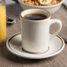 A Tuxton brown speckle tiara mug filled with coffee on a saucer with a bowl of cereal and a glass of orange juice.