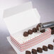 A 1 lb. Valentine's Day heart candy box on a counter with tongs holding a chocolate.