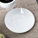 A white Libbey porcelain espresso saucer holding a cup of coffee on a table.