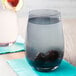 A Stolzle smoky grey stemless wine glass filled with water and blackberries on a white background.