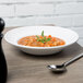 A Libbey bright white porcelain soup bowl with a spoon in it on a table.