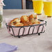 A Clipper Mill black iron oval wire basket filled with muffins on a table.