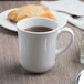 A Libbey tall porcelain cup filled with coffee on a table with a pastry.