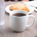 A Libbey bright white porcelain mug filled with coffee on a table with pastries.