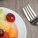 A Libbey bright white porcelain fruit bowl filled with fruit with a fork next to it.