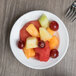 A table with a Libbey Orbis bright white porcelain fruit bowl filled with fruit.