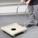 A man using a chrome-plated handle to push a beige Vollrath dish rack dolly.