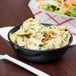 A bowl of pasta and a Solo black wide sauce cup on a plate with salad.