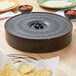 A circular black Carlisle tortilla server on a table with tortillas and salsa.