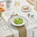 An Acopa stainless steel iced tea spoon on a white table with a plate of food.