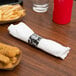 A Hoffmaster white linen-like napkin and clear plastic cutlery set wrapped in a napkin on a table with french fries and a red cup.