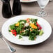 A Libbey medium rim porcelain plate with salad, vegetables, and cheese with a fork on a white table.