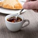 A hand holding a spoon in a Libbey Bright White Porcelain espresso cup of liquid.