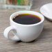 A Libbey bright white porcelain espresso cup on a table with a cup of coffee.