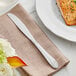 An Acopa Monaca stainless steel dinner knife on a napkin next to a plate of food.