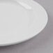 A close up of a Libbey bright white porcelain plate with a medium rim on a gray surface.