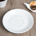 A Libbey Basics bright white saucer with a tea bag on a wooden table.