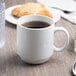 A Libbey bright white porcelain stacking mug filled with coffee on a table.