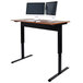 A Luxor pneumatic adjustable height standing desk with a computer and two monitors on it.