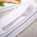 A Bon Chef stainless steel dinner fork on a napkin next to a plate of food.