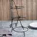 A Clipper Mill black metal 3-tier pizza stand on a table.