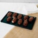 A Tablecraft hunter green cast aluminum rectangular cooling platter with chocolate covered donuts on it.