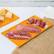 Two orange Tablecraft cast aluminum rectangular cooling platters with meat and cheese on them.