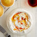 A bowl of whipped cream with caramel sauce and a cupcake with yellow food coloring on top.