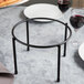 A black metal Clipper Mill 1-tier pizza stand on a table with plates and wine glasses.