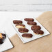 A Tablecraft white cast aluminum rectangular cooling platter with chocolate covered donuts on it.