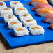 A Tablecraft cobalt blue cast aluminum rectangular platter with sushi on it.