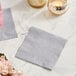 A set of gray Choice 2-ply beverage napkins on a marble table with candles.