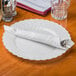 A white plate with a silver knife and fork on a silver Hoffmaster dinner napkin.