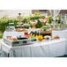 A Tablecraft translucent clear metal table cover on a table with food and drinks.