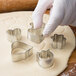 A person's gloved hand using a Wilton metal heart-shaped cookie cutter.