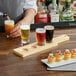 A man using an Acopa natural wood flight paddle to serve beer at a bar.