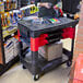 A person standing at a store with a Rubbermaid black TradeMaster cart.