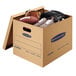 A Banker's Box medium moving box filled with sports equipment including a baseball glove and football.