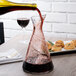A Stolzle Pisa carafe being filled with red wine from a glass.
